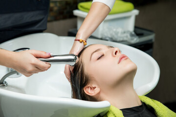 young woman with hairdresser washing head at hair salon