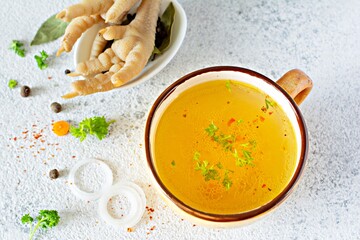 Homemade chicken (bone) broth/bouillon with vegetables, spices and herbs in a bowl (cup) on a light background. Natural collagen of animal origin. Liquid broth from meat, fish, vegetables.