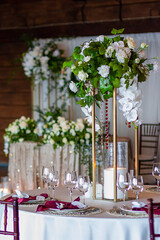 A white and green bouquet of flowers in a golden vase stands on a festive table close-up.  Served table