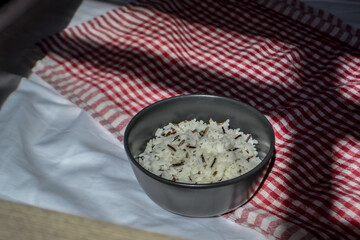 white parboiled black rice in dark cup on plate on red-white cloth towels under the light of the sun with shadow on table