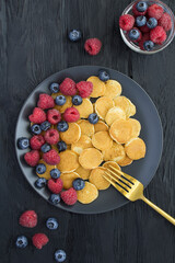 Top view of mini pancakes with berries  in the black plate on the dark  background