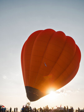 A crowd of people launches a huge orange balloon into the sky