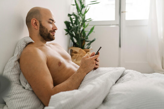 Young handsome man using his mobile phone in the bed