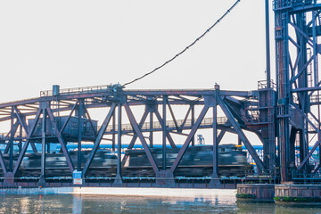 Blurry train speeding through steel bridge over river in city