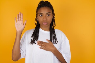 Young dark skinned woman with braids hair wearing white t-shirt over yellow background Swearing...