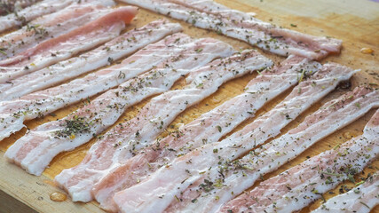 sliced raw bacon on a Board in spices. with pepper oil, herbs. delicious food.