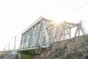 metal railway bridge over a small river, selective focus, tinted image, rays of the rising sun