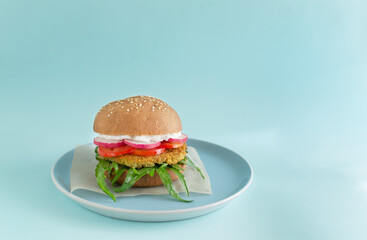 Vegetarian burger with chickpea cutlet and vegetables on a blue background. Vegetarian food concept. Copy space.