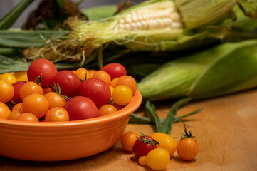 Small multicolored tomatoes with corn on the cob in background