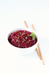 Korean beetroot salad with garlic and parsley in a bowl with wooden sticks on a white background