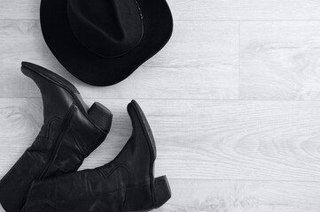 Black cowboy boots and black hat on gray wooden background.