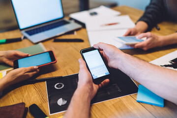 Colleagues sitting at desk and interacting with smartphones in modern office