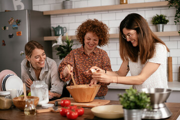 Girlfriends having fun in kitchen. Sisters preparing delicious food at home