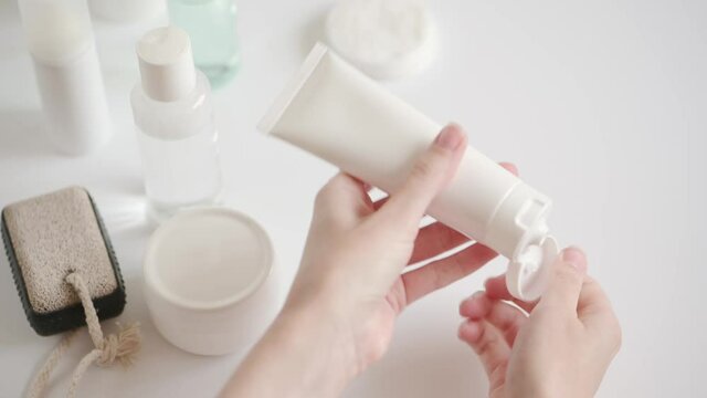 The girl takes a plastic package with cream and squeezes the cosmetic product onto her hands. Rubbing moisturizer to moisturize the skin. Home skincare in quarantine, isolation
