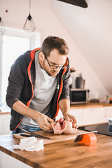 Fototapeta na wymiar attractive nerd guy with glasses in stylish kitchen follows a recipe on the phone prepares chicken