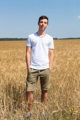 Handsome teen age fellow with hands in pockets standing on an agricultural field, full-length portrait