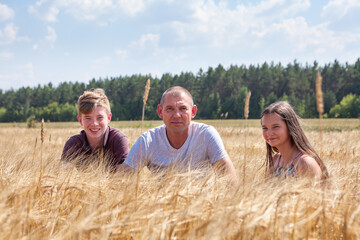 Calm adult single father with his smiling preteen children sitting in wheat stems,