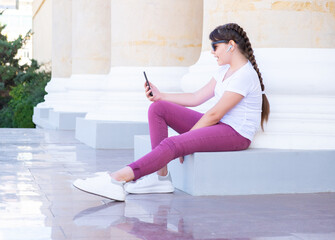 Urban stylish teenager girl makes video call on mobile phones, uses hands free, talks with friends.