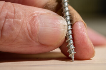 Macro of a man holding a screw in his fingers as he prepares to screw it into a board