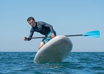 Man surfing on inflatable stand-up paddle board at summer sunny day. Extreme sport activity
