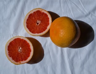 cut bright red orange grapefruit and whole on white cloth with folds in light of sun with shadows