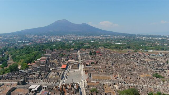 Aerial view of ruins of Pompeii, ancient Roman city destroyed by volcanic eruption of volcano Mount Vesuvius, cone of Mount Vesuvius in background, clear blue sky - Naples, Campania, Italy, Europe