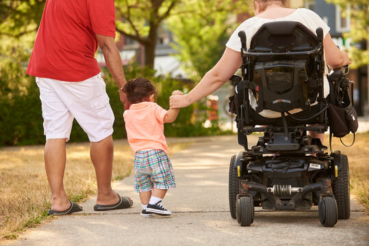 Rear view of disabled mother and father holding child's hand as he learns to walk.