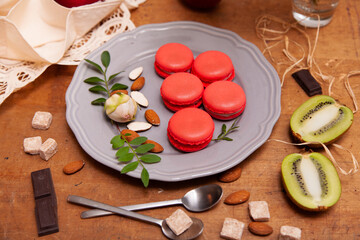 Five macaroons on a grey plate wuth almonds, pieces of broun shuger, chocolate and kiwi
