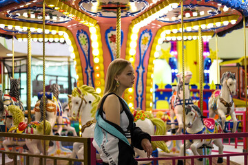 Beautiful stylish girl stands near the carousel in the amusement park