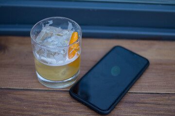 Whiskey sour and black smartphone on wooden table