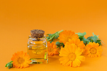Natural Cosmetic oil with a calendula flowers on orange background. Healthy skin care. Aromatherapy, spa and wellness concept - obrazy, fototapety, plakaty
