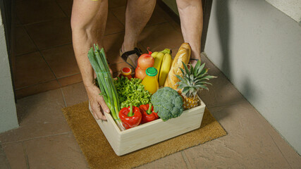 CLOSE UP: Senior lady lifts a box full of organic groceries left on her doormat.