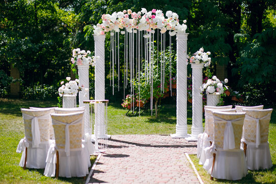 wedding day, white arch for the wedding ceremony and chairs against a background of green trees stand on a green lawn on the eve of the bride and groom's release, free space for text, sunny day