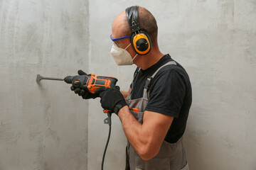 hand of the builder holds an hammer drill on background of gray wall with copy space