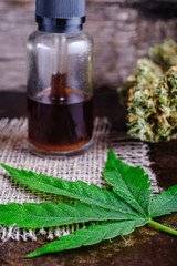 brown medical cannabis resin extract in bottle of medicine dropper. next to marijuana buds and hemp leaf. on hemp sack. Wooden backdround on rust metal suface. vertical