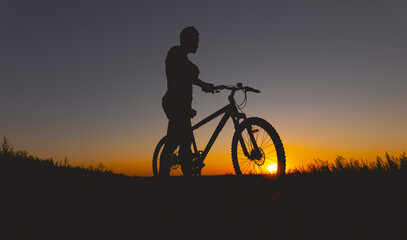 Silhouette of a man standing with mountain bike at sunset