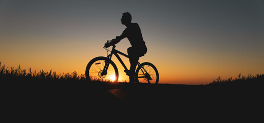 Fototapeta na wymiar Silhouette of a man mountain biker at sunset riding bicycle