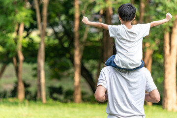 Dad giving son ride on back in the park. Asian family cute and warm. Father and child having fun outdoors.