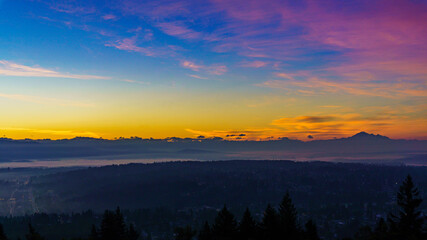 Early morning mists rising off valley floor as new day dawns above mountains in silhouette
