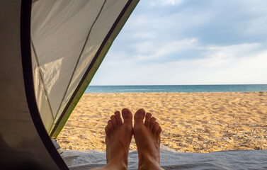 pair of woman feet on the background of a sandy beach and the sea. View from the tent. Outdoor activities. Summer time in nature