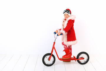 A cute little boy like Santa Claus is riding a red kick scooter. White background.