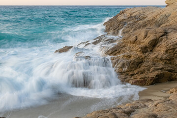 Long exposure time image shore in beach with water flowing from the stones in Ikaria, Island in the Aegean Sea, Greece