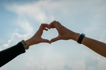 close up male and female hands making a heart shape silhouette in the sky.