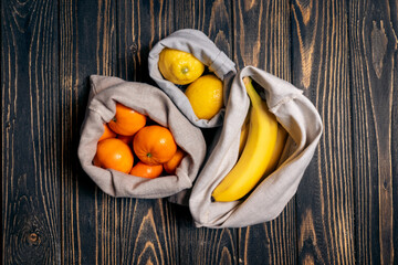 fresh fruits in recyclable eco bags on wooden table, top view