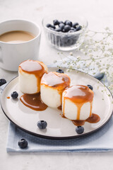 Fritters of cottage cheese with caramel sauce, blueberries, in plate, light background, vertical format.
