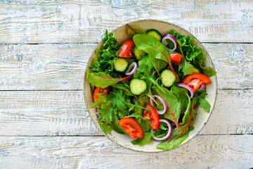 Salad with tomatoes, cucumbers and various green leaves, on white wooden boards.