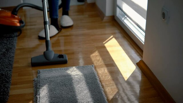 Beautiful woman is hoovering the parquet floor at home using modern vacuum cleaner
