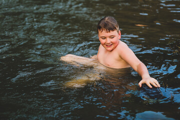 Boy swimming in river at dusk with big smile. Moody image with rich tones
