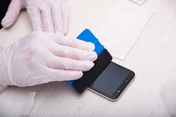a man in rubber gloves glues a protective glass to a smartphone using a special palstic spatula with a soft nozzle