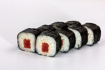 A tuna roll in nori lies on a shiny white Board